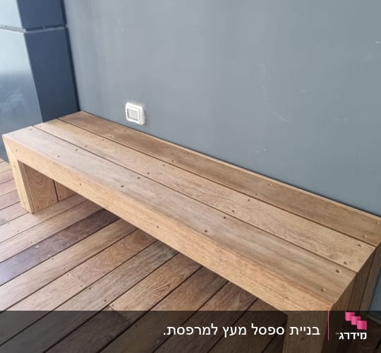 ספסל עץ על רצפת דק ליד קיר אפור